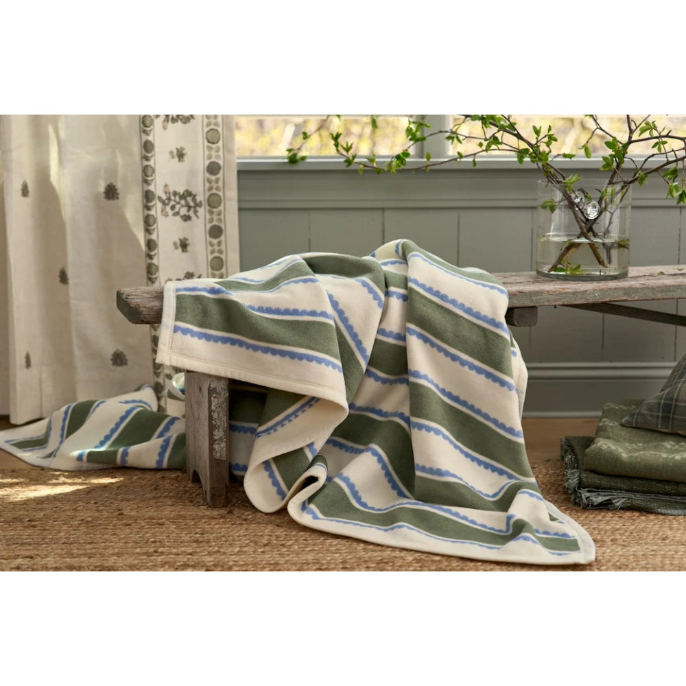 A soft woven throw blanket with green, cream, and blue stripes draped over a rustic wooden bench in a styled room setting.