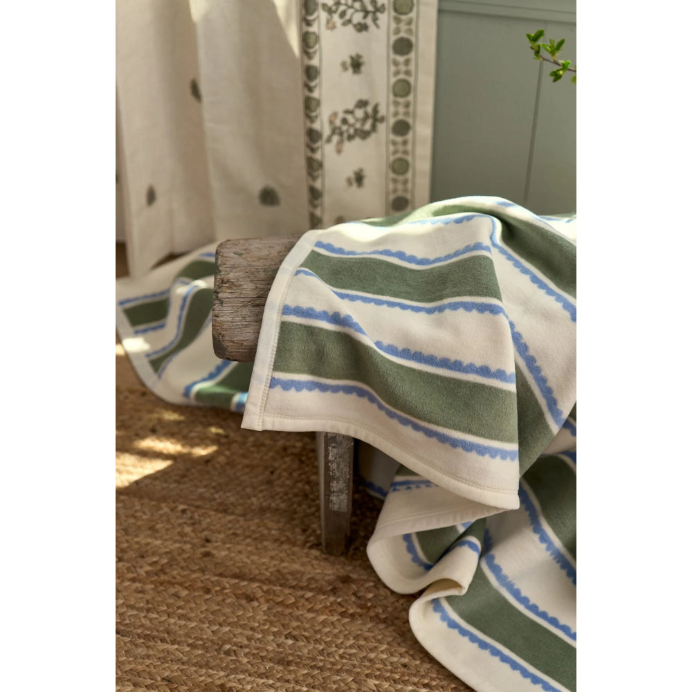 A striped throw blanket draped over a rustic wooden chair in a home setting, featuring green, blue, and white horizontal stripes.