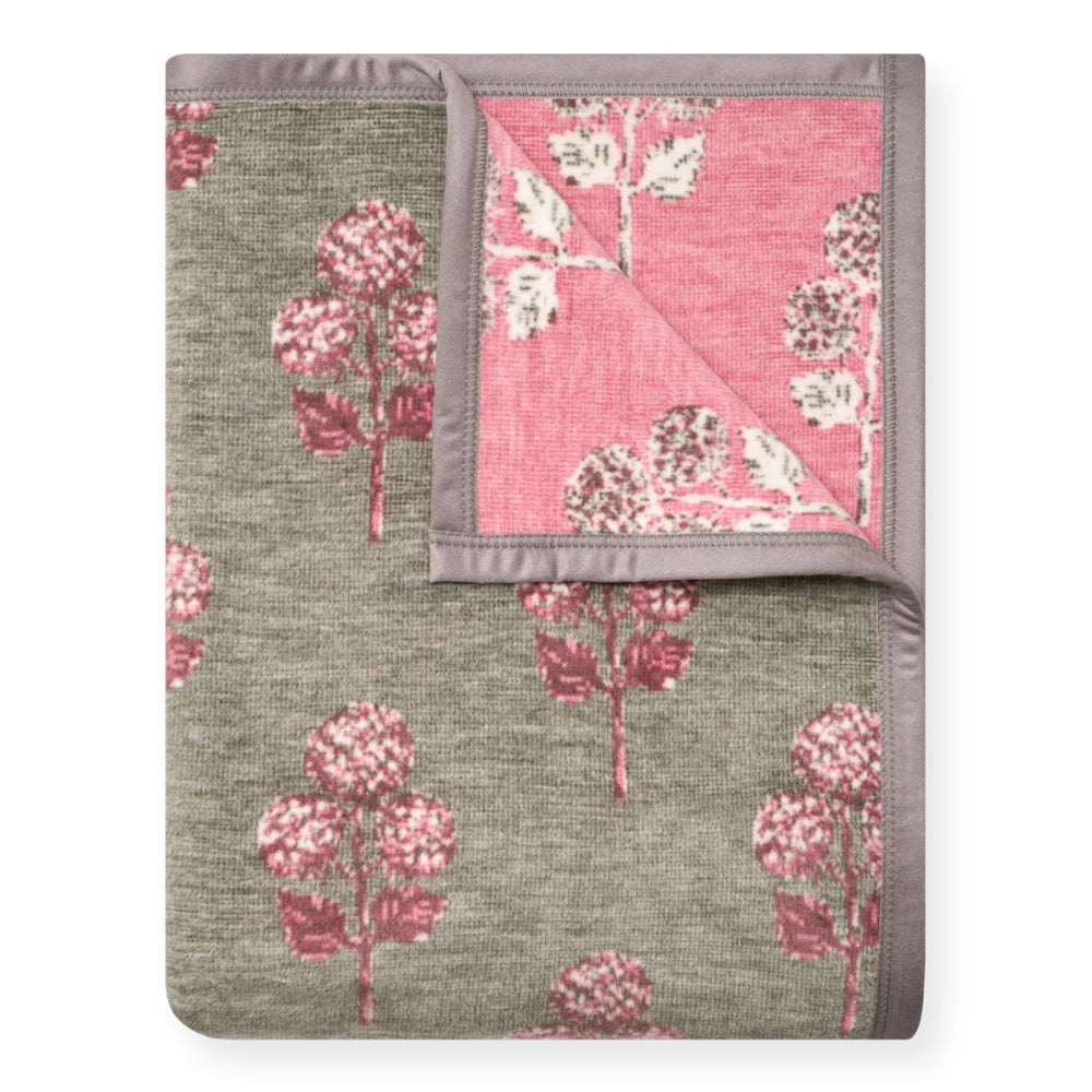 A folded throw blanket with a textured sage green and dusty pink floral pattern, featuring a solid pink reverse side with white floral motifs and a gray border.