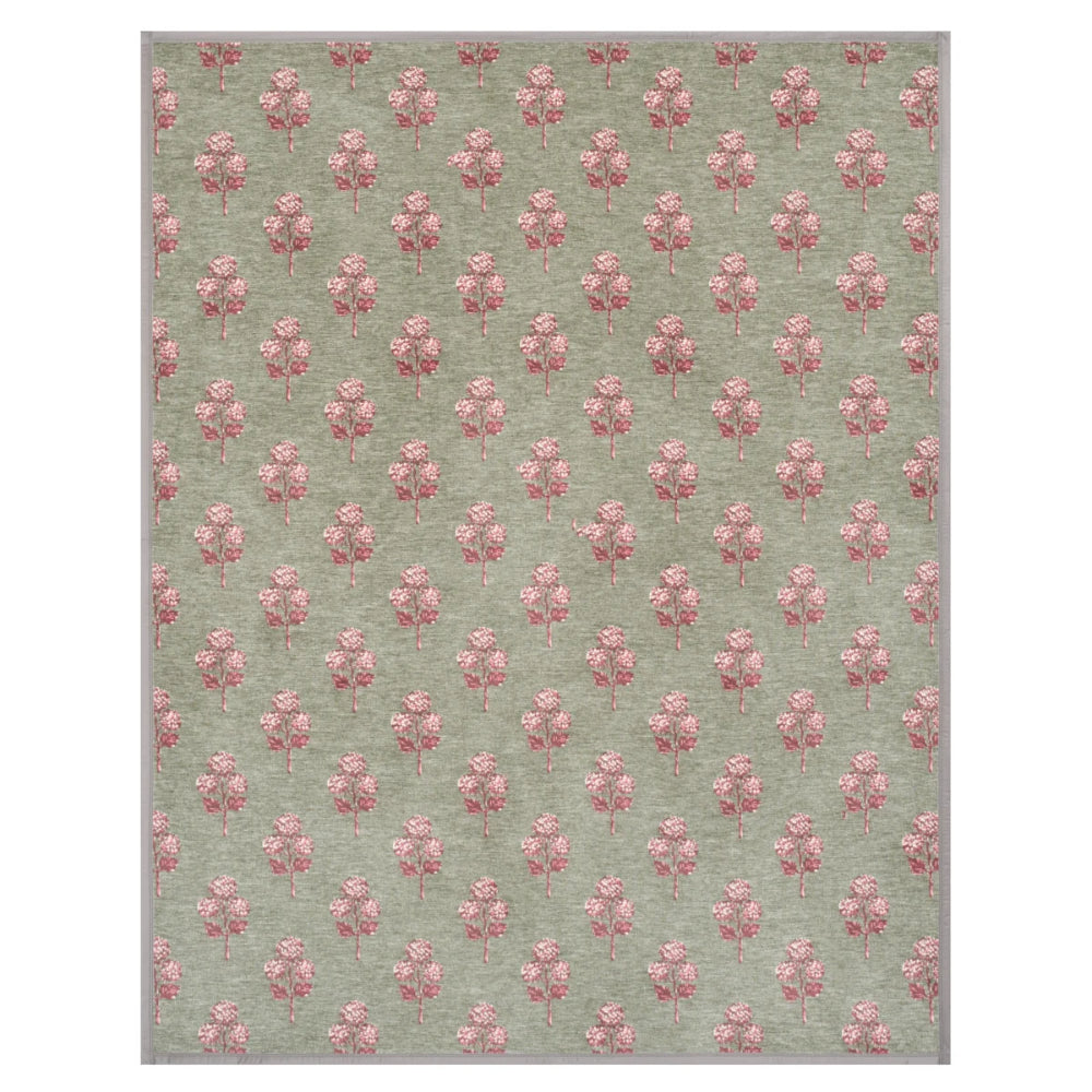 A rectangular area rug with a repeating pattern of pink floral motifs on a muted sage green background.
