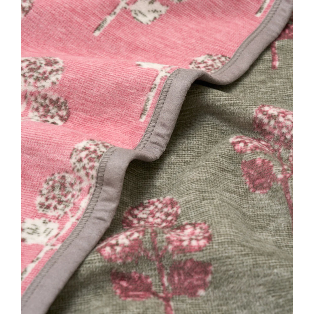 A close-up of a folded textile product showing two patterned fabric sides: one pink with white floral motifs and one muted olive green with pink floral motifs, separated by a gray stitched border.