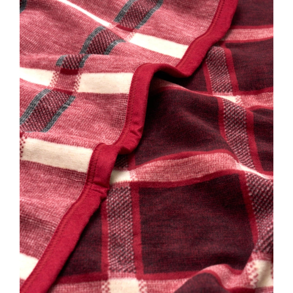 A close-up of a plaid blanket or throw with a deep red and cream pattern, featuring a solid red stitched border.