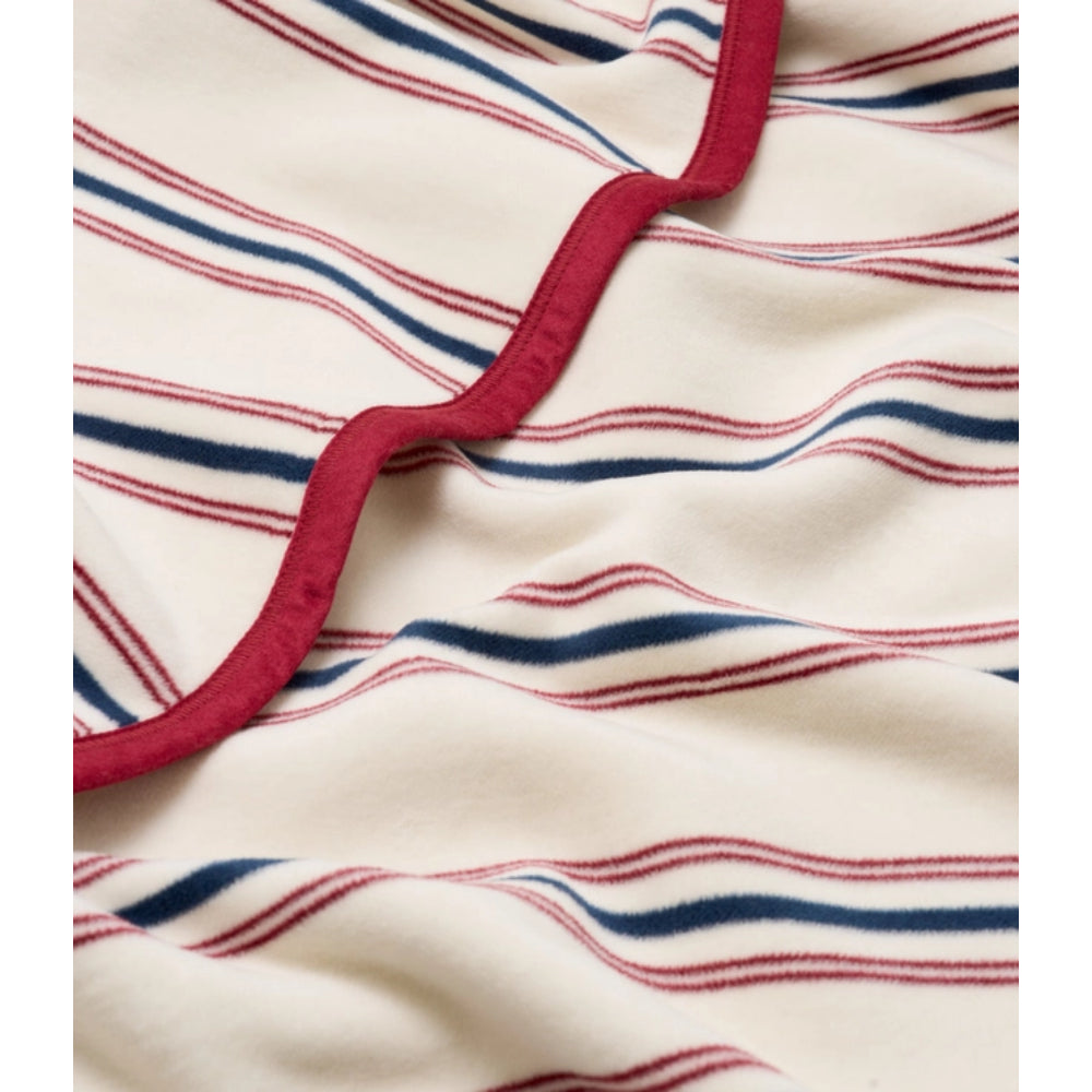 Close-up of a striped fabric product, likely a blanket or throw, featuring an off-white base with thin red and navy blue wavy stripes and a prominent scalloped red border.