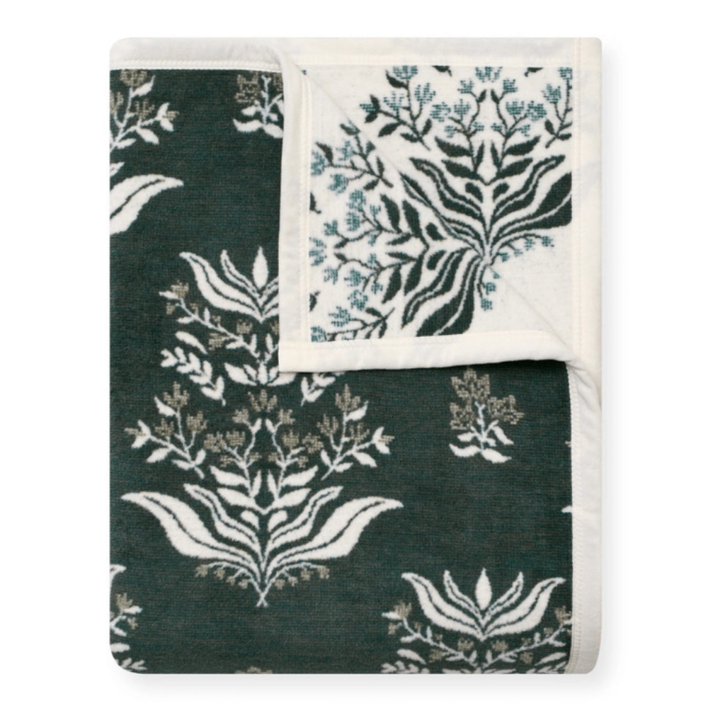 A folded throw blanket featuring a dark forest green and white botanical damask pattern, with a folded corner revealing an off-white reverse side with a light blue botanical print.