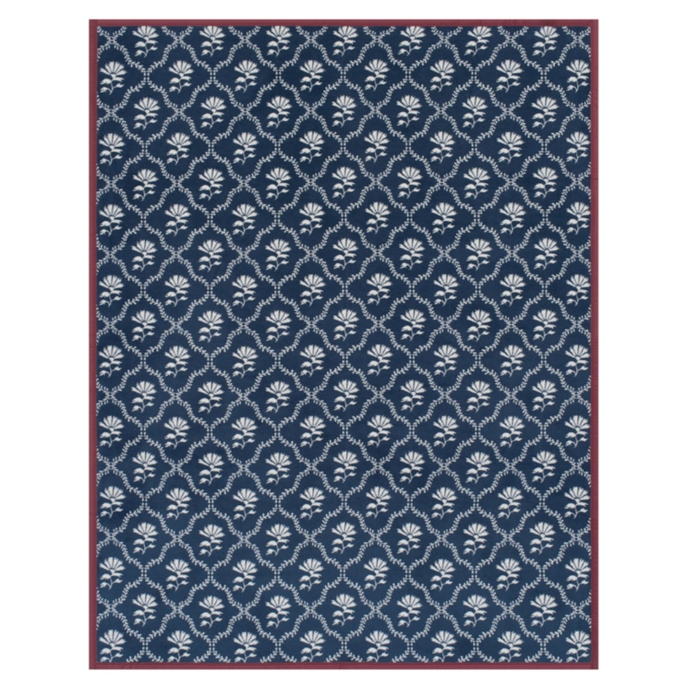A rectangular blanket with a navy blue background, featuring a repeating white floral and geometric lattice pattern, finished with a solid dark red border.
