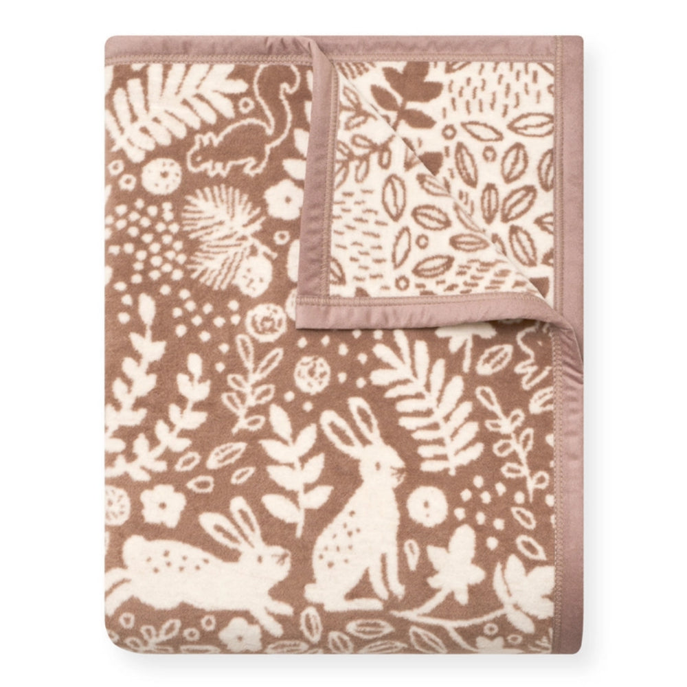 A folded fleece blanket with a brown and cream woodland pattern featuring rabbits, leaves, and pinecones, with a solid brown border.