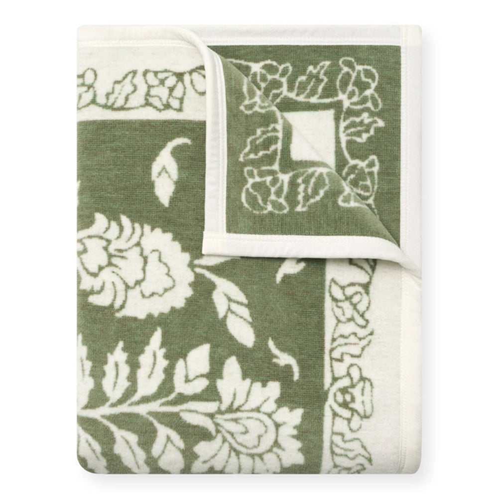 A folded green and white patterned textile, likely a blanket, throw, or towel, shown on a clean white background. The fabric features a floral and botanical motif with a decorative border.