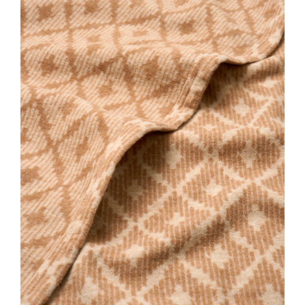 A close-up of a soft woven textile with a tan and cream geometric diamond pattern, draped to show its texture and folds.