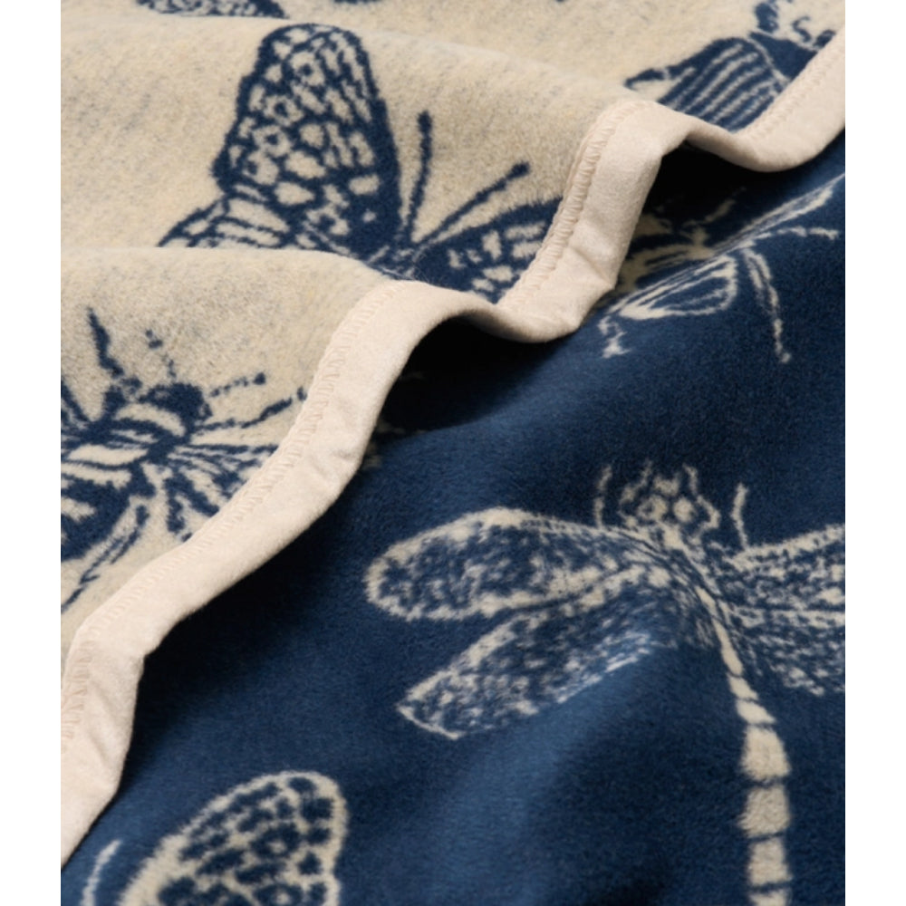 A close up of a Midi Blanket with cream and blue colors and bug designs. 