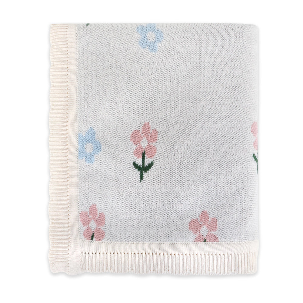 A folded knit baby blanket with cream-colored ribbed borders and a pattern of small pink and light blue flowers with green stems on a white background.