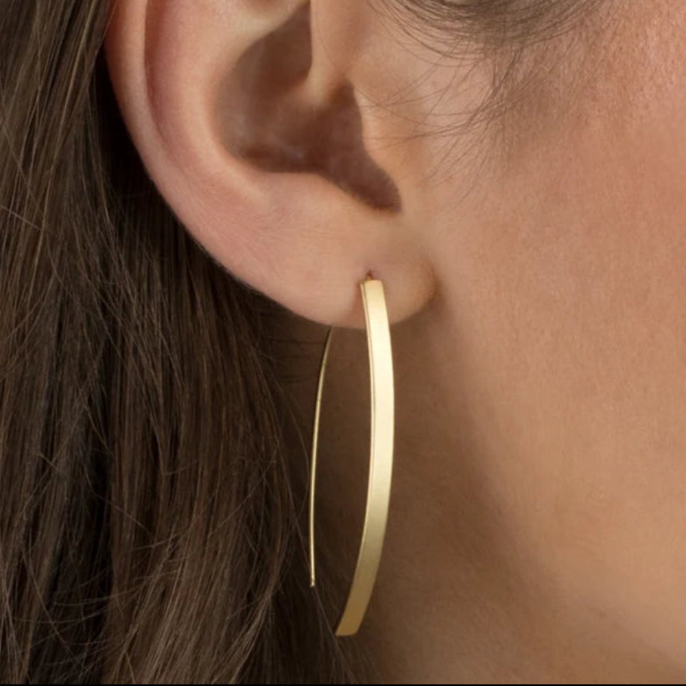 A close-up of a model's ear wearing a minimalist, thin gold hoop earring.