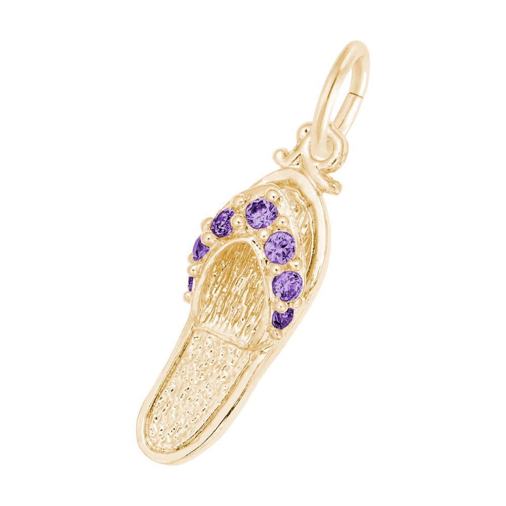 A gold charm shaped like a flip-flop sandal, featuring textured gold detailing and a row of round purple gemstones along the strap, set against a plain white background.