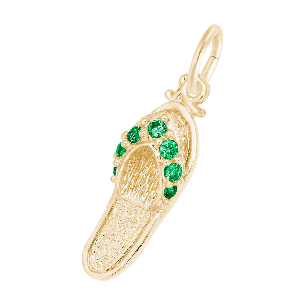 A gold charm shaped like a flip-flop sandal, featuring textured gold detailing and a row of round green gemstones along the strap, set against a plain white background.