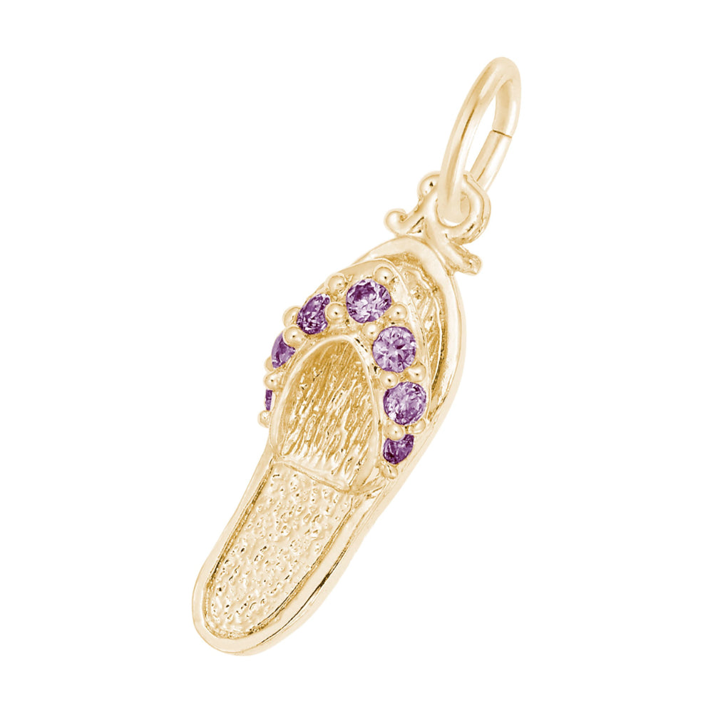 A gold charm shaped like a flip-flop sandal, featuring textured gold detailing and a row of round purple gemstones along the strap, set against a plain white background.