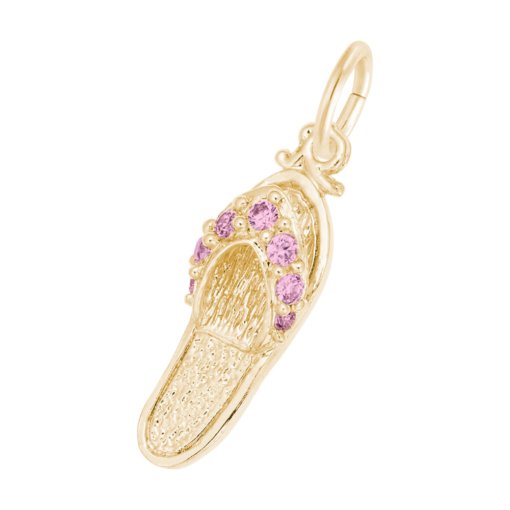 A gold charm shaped like a flip-flop sandal, featuring textured gold detailing and a row of round pink gemstones along the strap, set against a plain white background.