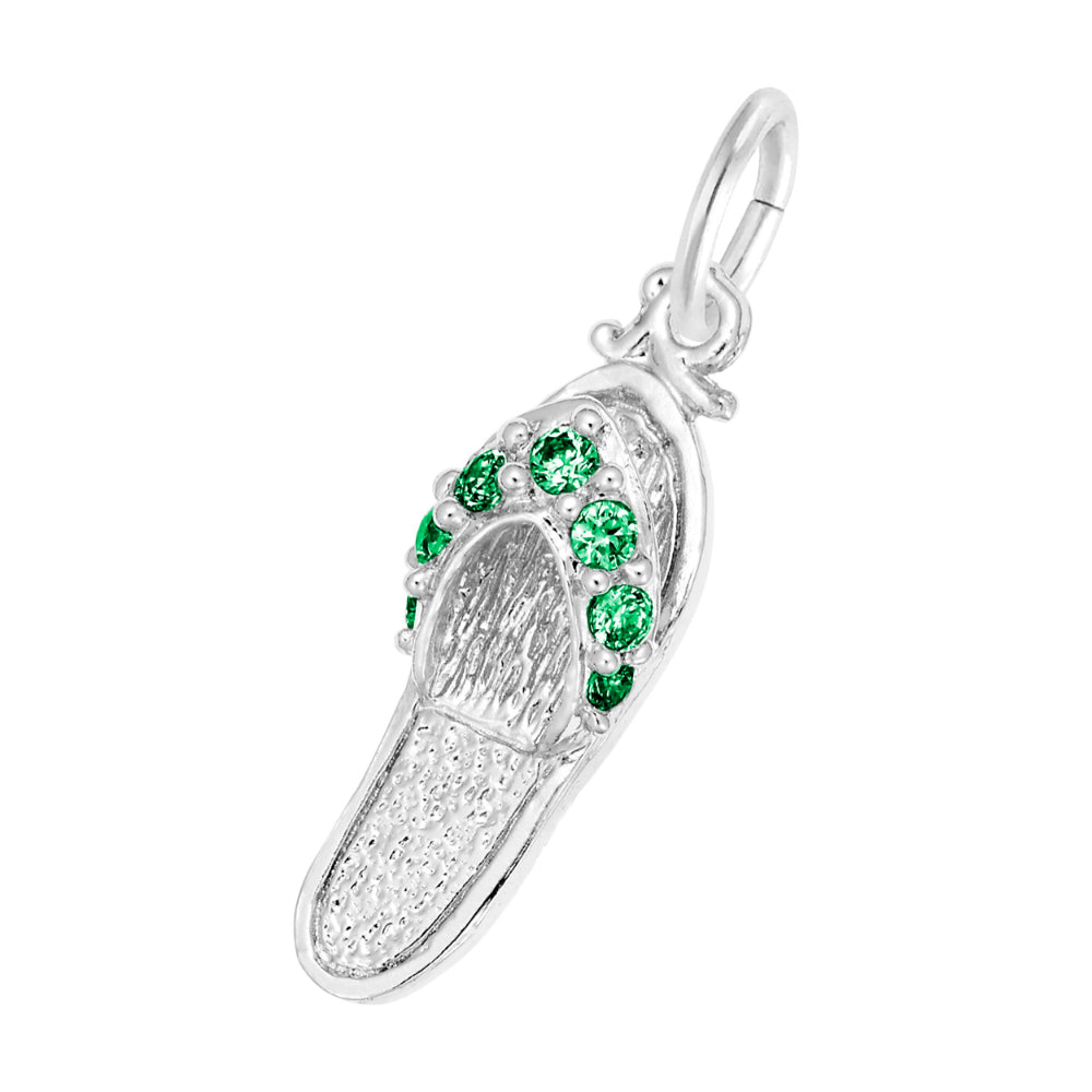 A silver charm shaped like a flip-flop sandal, featuring textured silver detailing and a row of round green gemstones along the strap, set against a plain white background.
