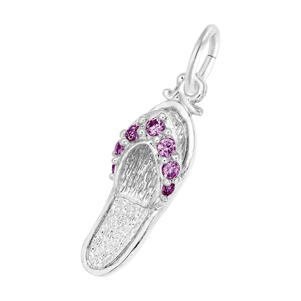 A silver charm shaped like a flip-flop sandal, featuring textured silver detailing and a row of round purple gemstones along the strap, set against a plain white background.