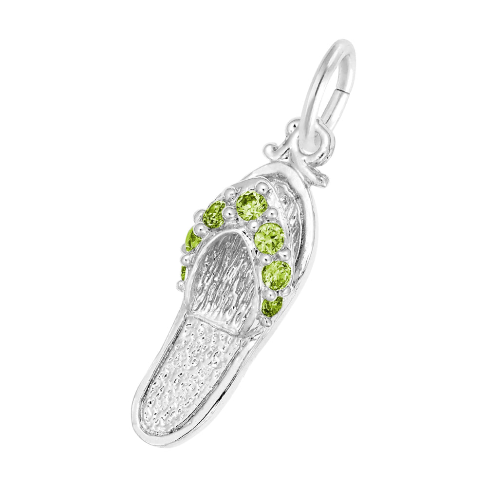 A silver charm shaped like a flip-flop sandal, featuring textured silver detailing and a row of round green gemstones along the strap, set against a plain white background.