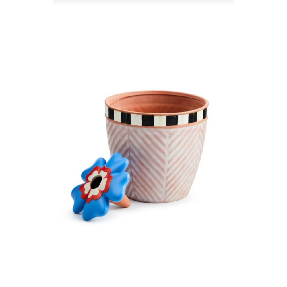 A beige MacKenzie-Childs Dolce Vita Self Care Planter with a geometric pattern and a small blue and red flower in it, placed against a white background.