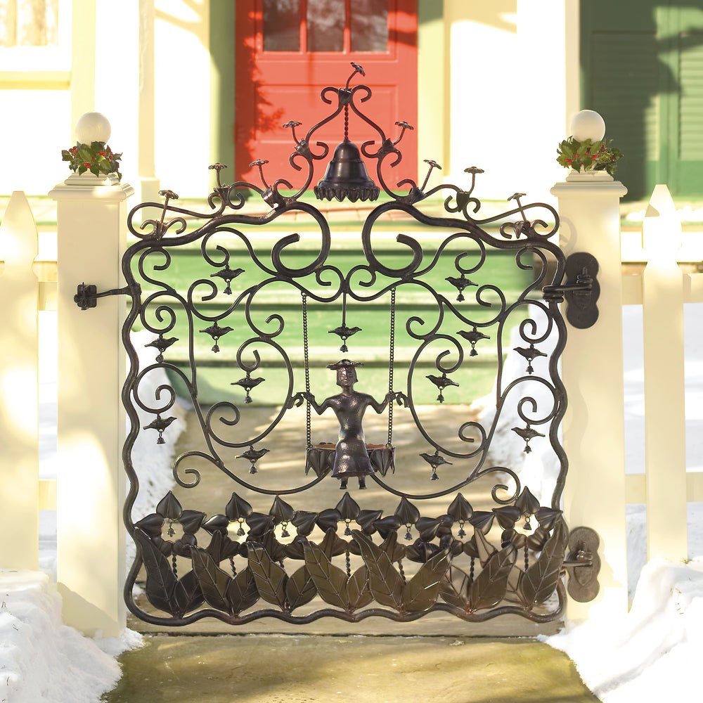 Decorative metal gate with intricate designs in front of a house with a red door.