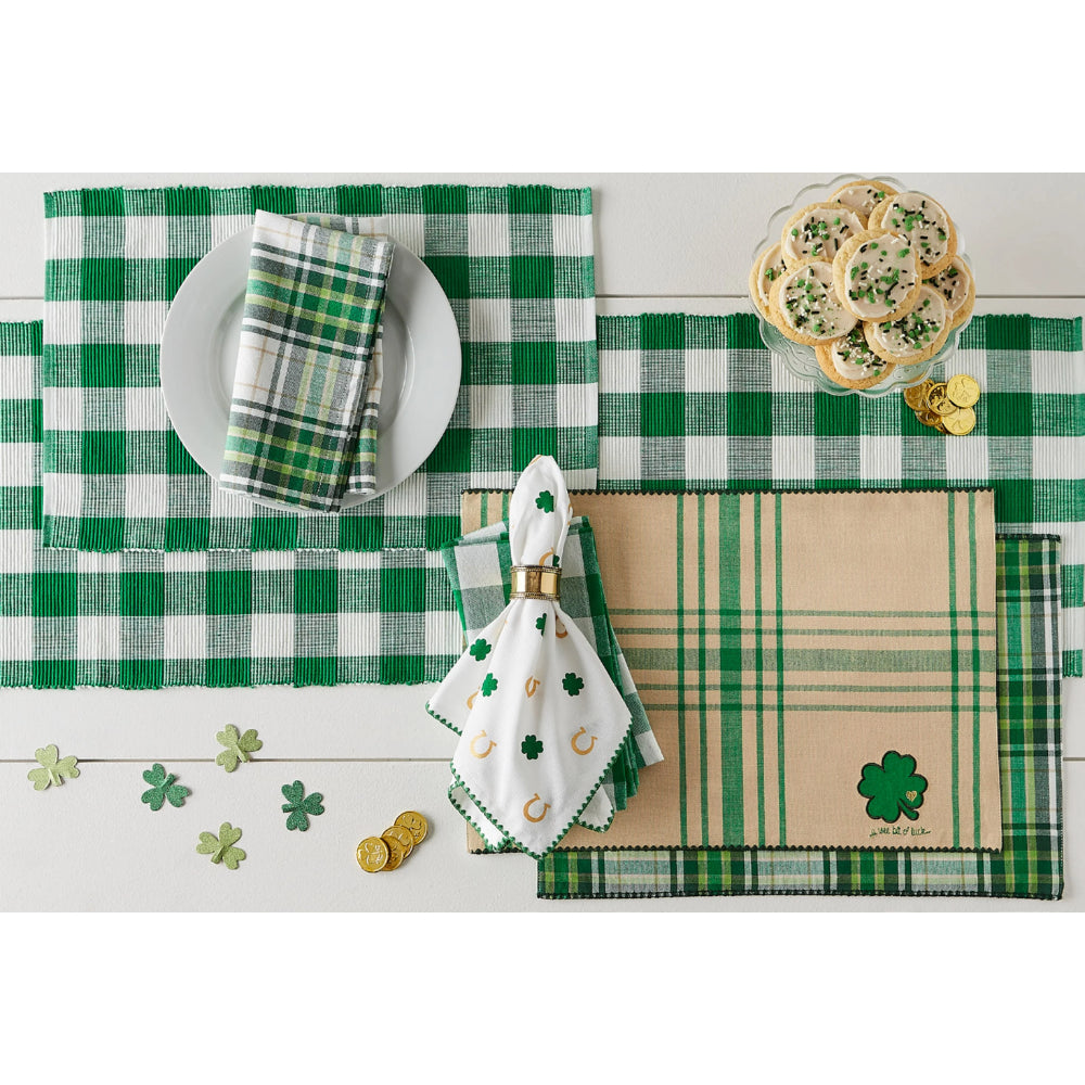 St. Patrick's Day-themed table setting with green checkered placemats, clover decorations, and gold coins on a white wooden surface.