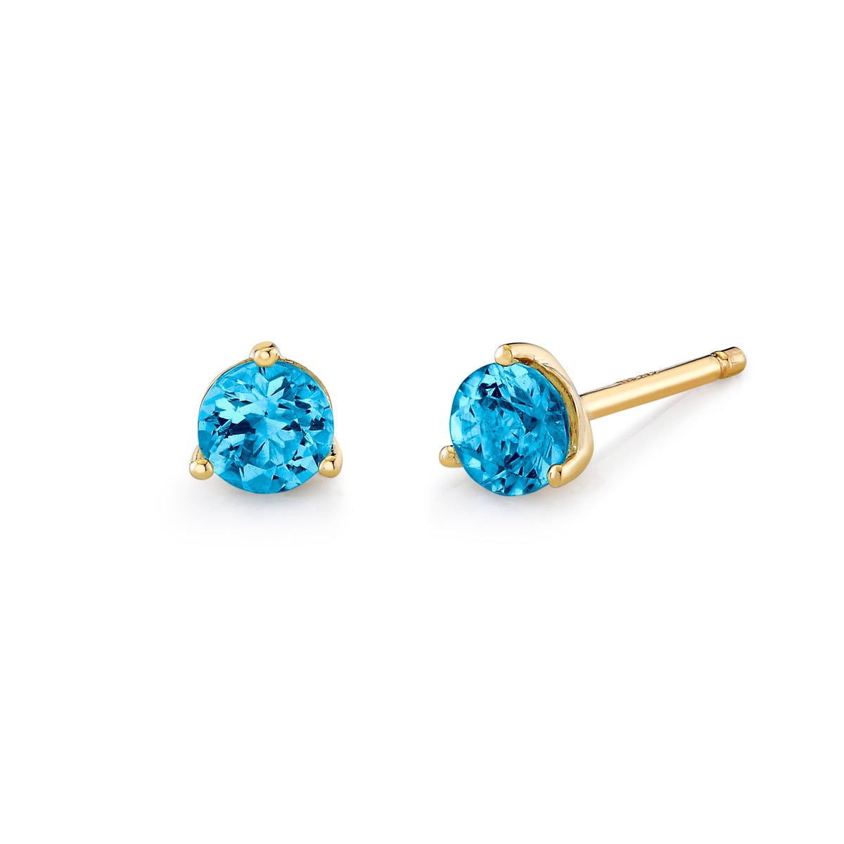 A pair of yellow gold stud earrings with round-cut bright blue gemstones, shown on a clean white background. One earring is facing forward to show the stone and prongs, while the other is angled to show the post and backing.