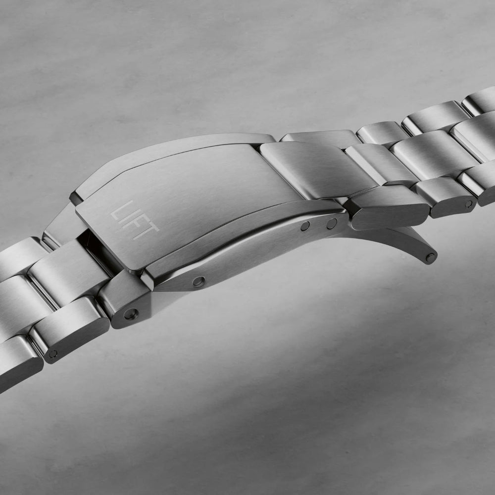 Close-up of a stainless steel watch band clasp with the brand name 'LIFT' engraved on the back, set against a neutral gray background.