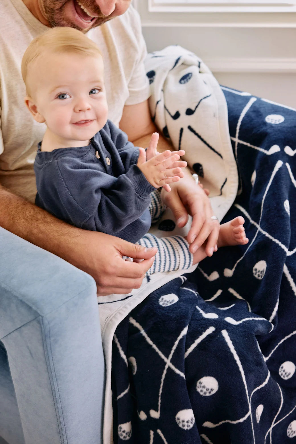 Baby sitting on a person's lap with a patterned golf blanket