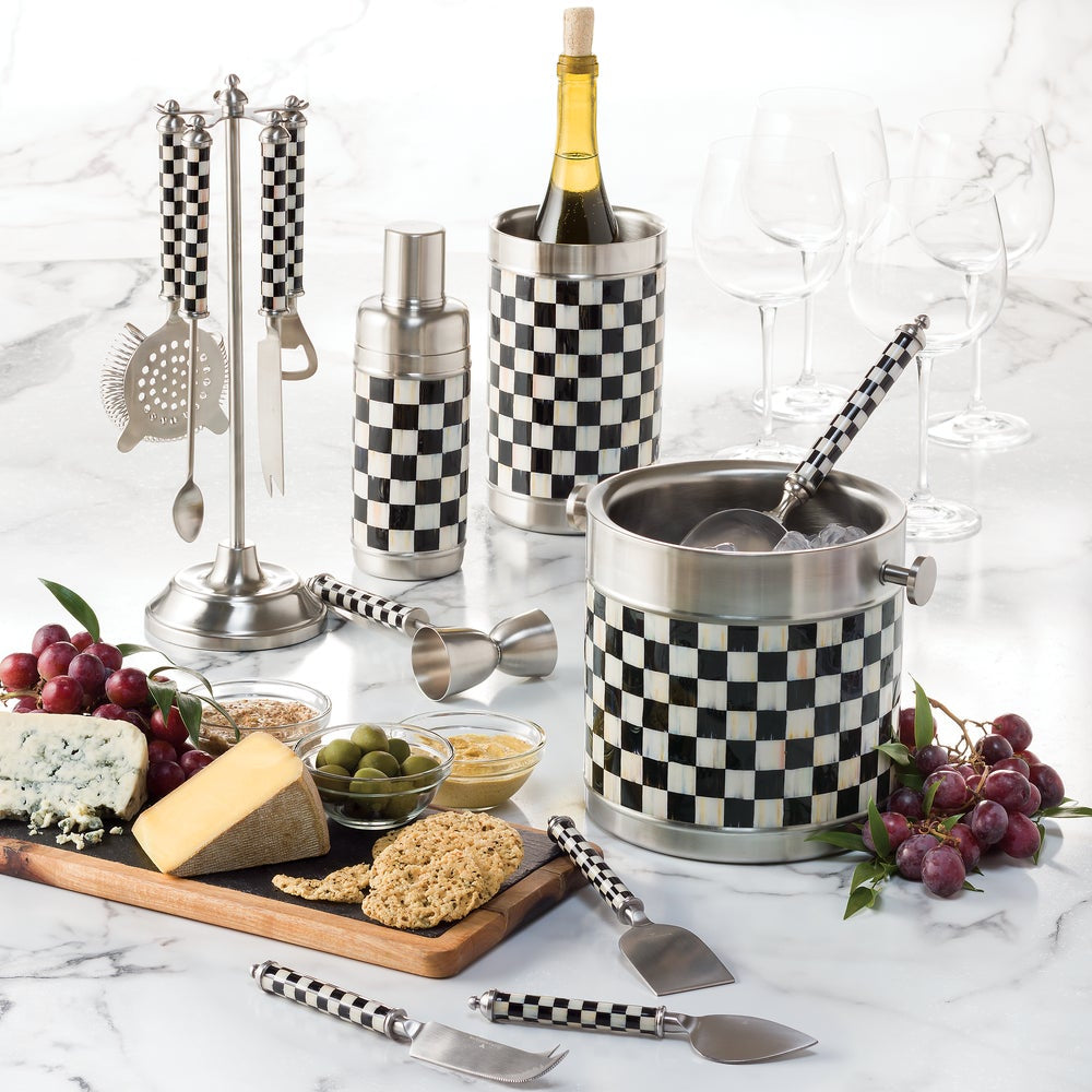 Gourmet set with checkered wine cooler, jigger, and cheese platter on a marble surface.