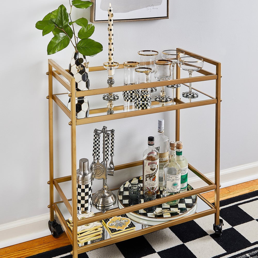 Gold bar cart with drinks and glasses on a checkered floor