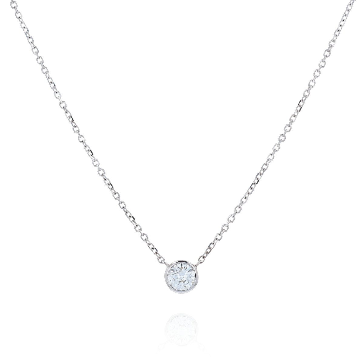 A delicate white gold chain necklace with a single round bezel-set diamond pendant, displayed on a clean white background with a soft reflection below.