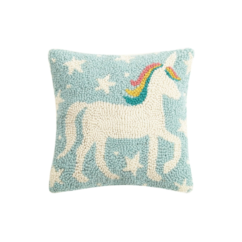 A square-shaped accent pillow with a woolen depiction of a unicorn in white and rainbow colors on a light blue background with stars.