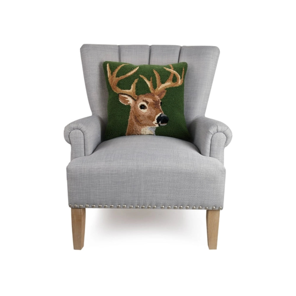 A light gray upholstered armchair with wooden legs and nailhead trim, shown against a white background with a green decorative throw pillow featuring a deer head design.