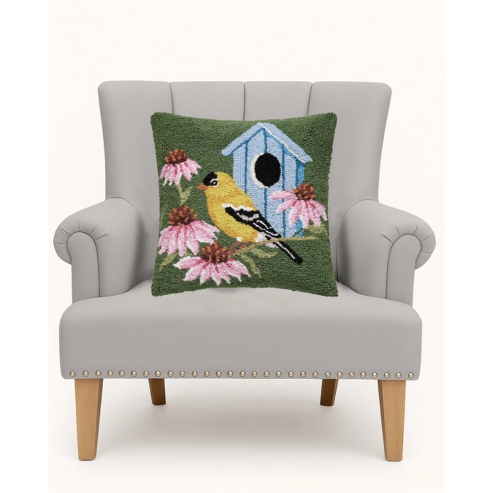Decorative pillow with bird and birdhouse design on a gray armchair.