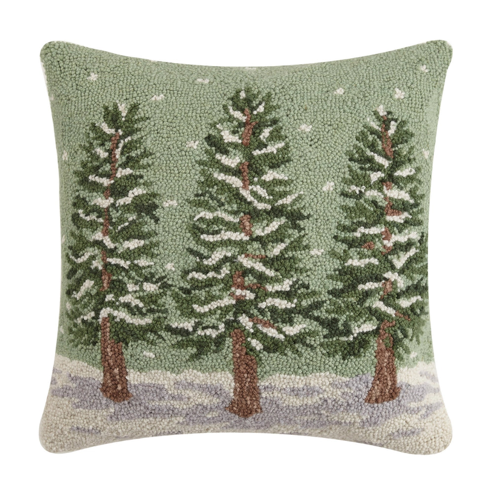 Rectangular throw pillow with a woolen depiction of three evergreen trees covered in snow on a green background, resembling a winter scene.