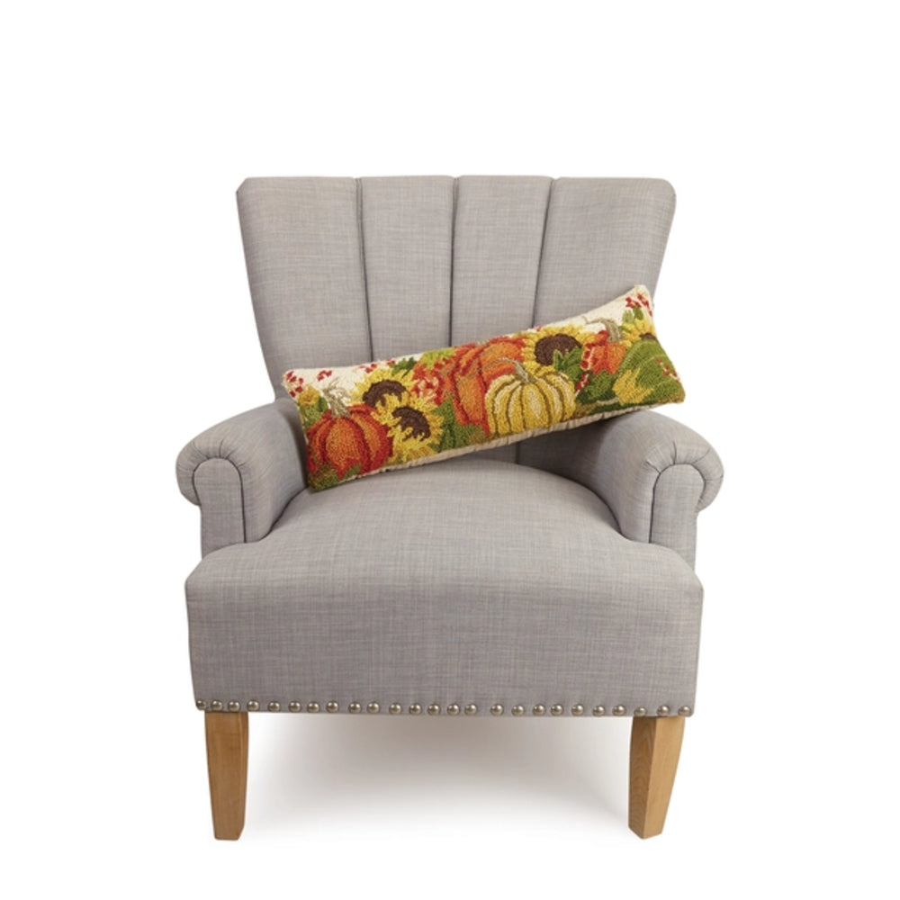 A light gray upholstered armchair with wooden legs and nailhead trim, styled with a long rectangular lumbar pillow featuring a colorful autumn pumpkin pattern, set against a plain white background.