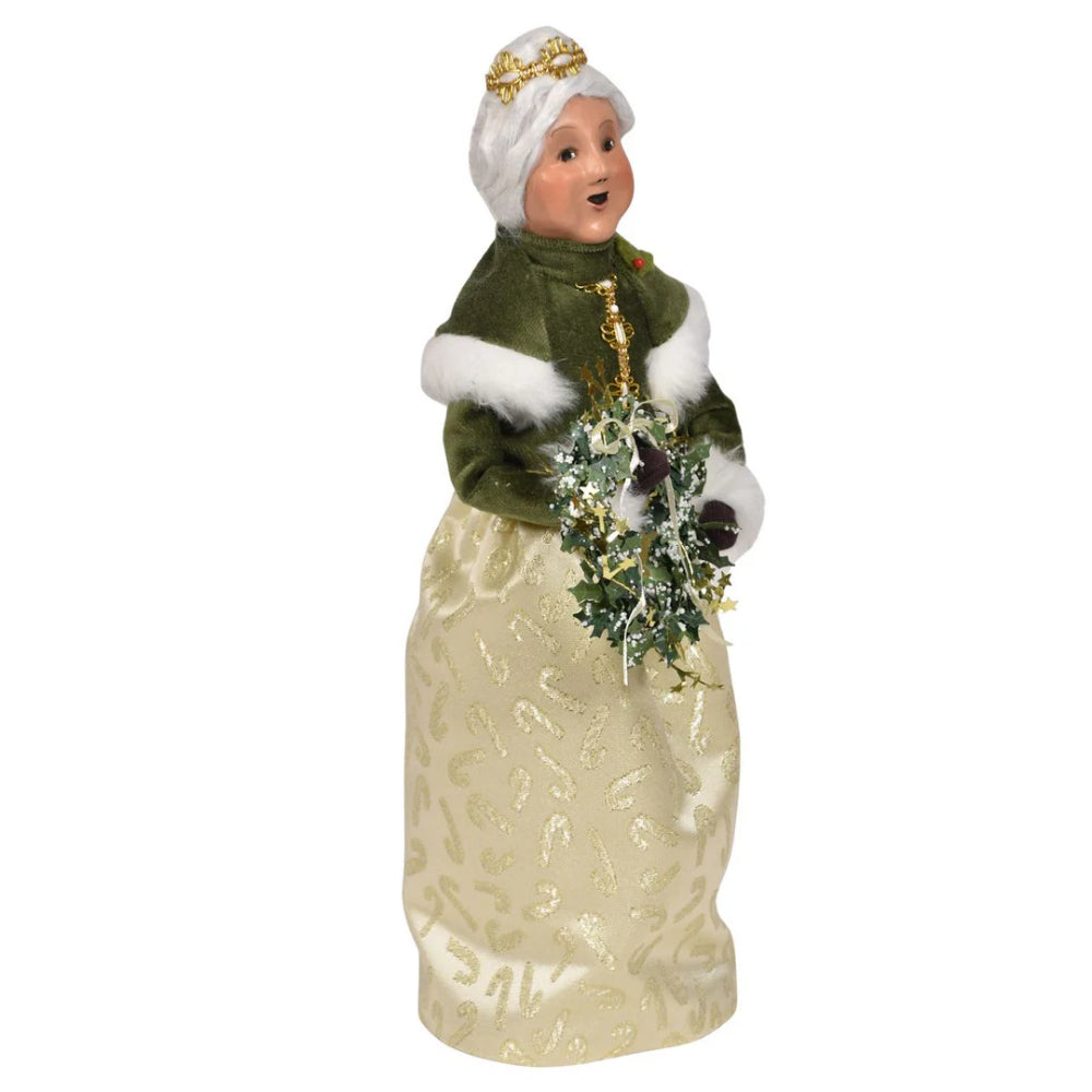 A second side angled photo of a gold and green decorative figurine of Mrs. Claus  holding a wreath on a white background