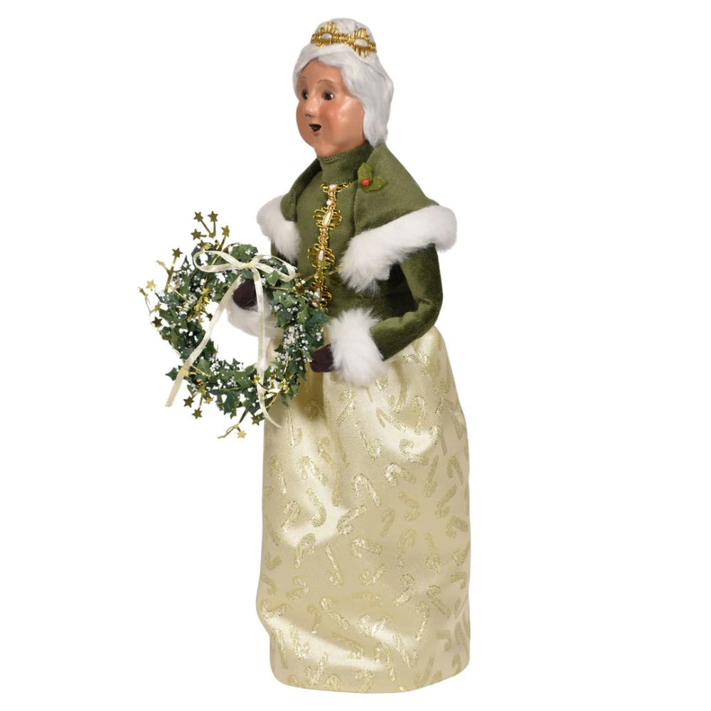 A side angled photo of a gold and green decorative figurine of Mrs. Claus  holding a wreath on a white background