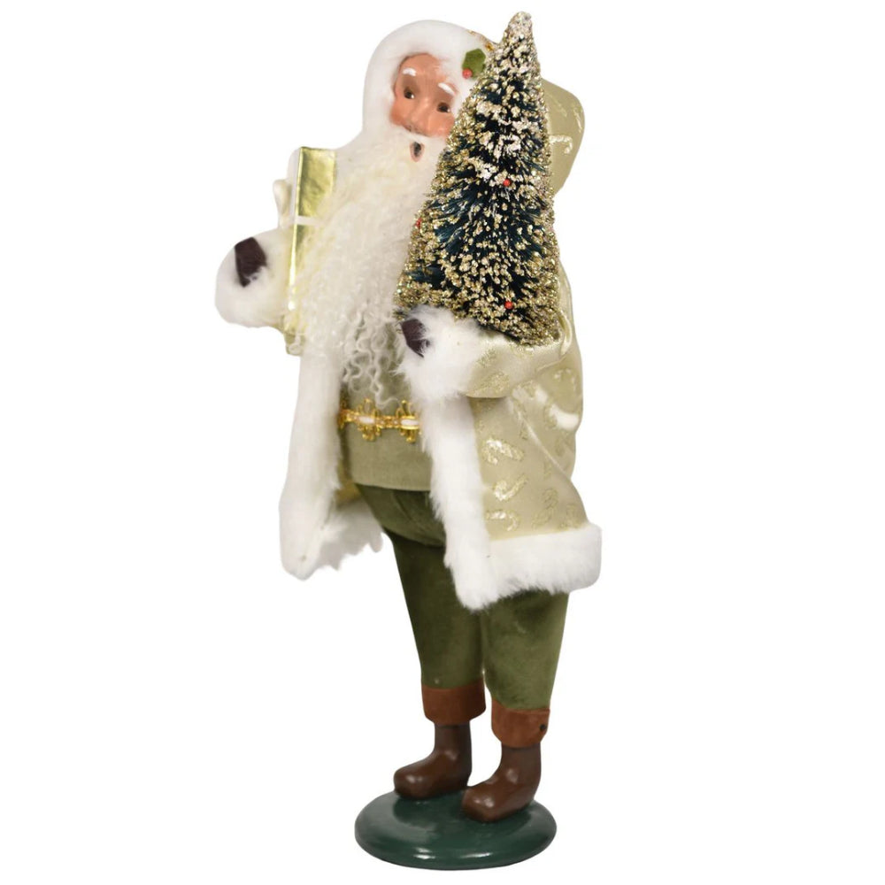 A side photo of a decorative figure of Santa with a, green and gold outfit, and holding a gift and tree on a white background.