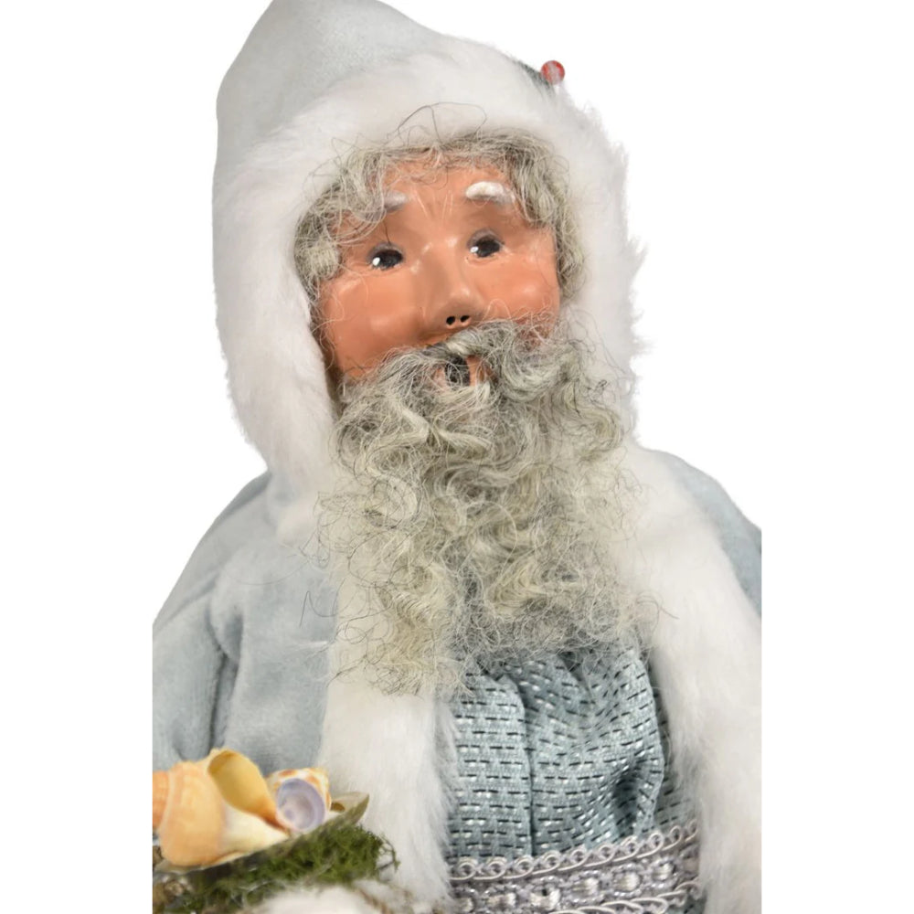 A close up photo of the face of the decorative figure of the Nautical Santa in a gray outfit with white fur trim, holding starfish and seaweed on a white background.