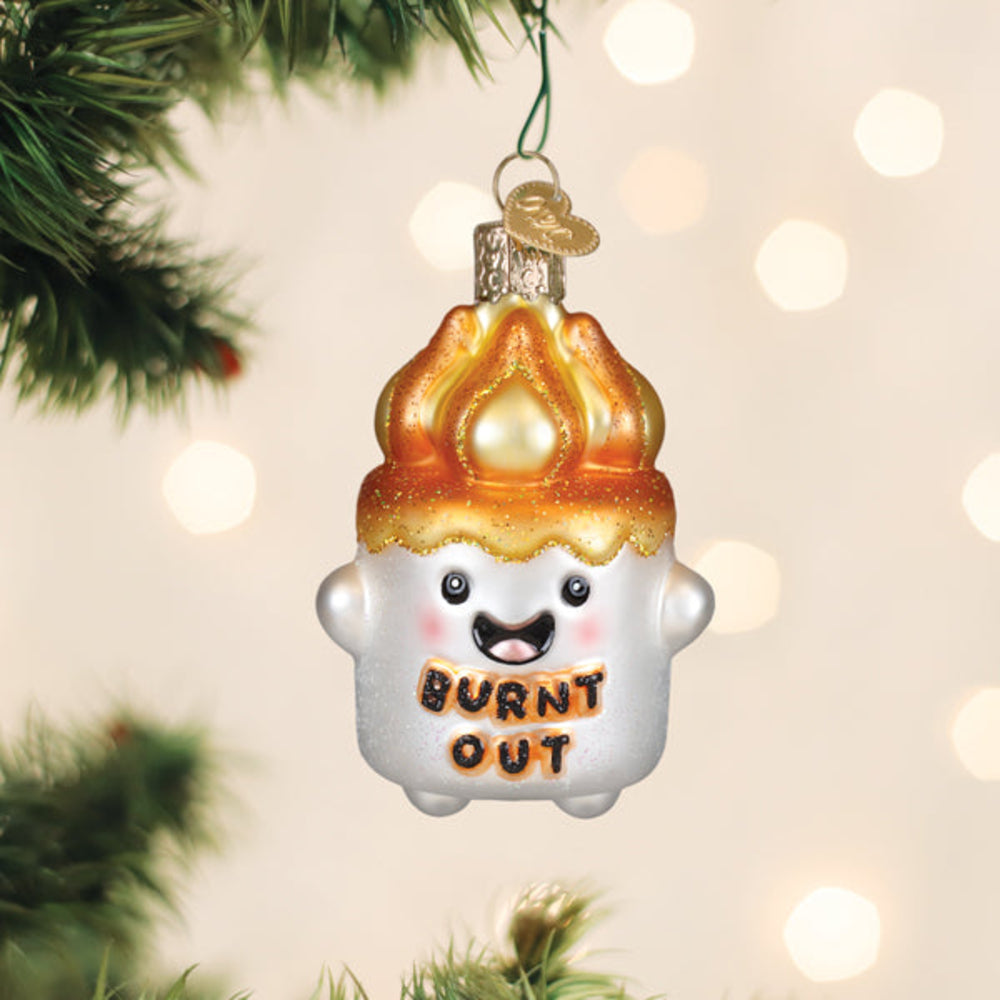 Glass ornament shaped like a burnt marshmallow with 'BURNT OUT' text, hanging on a Christmas tree.