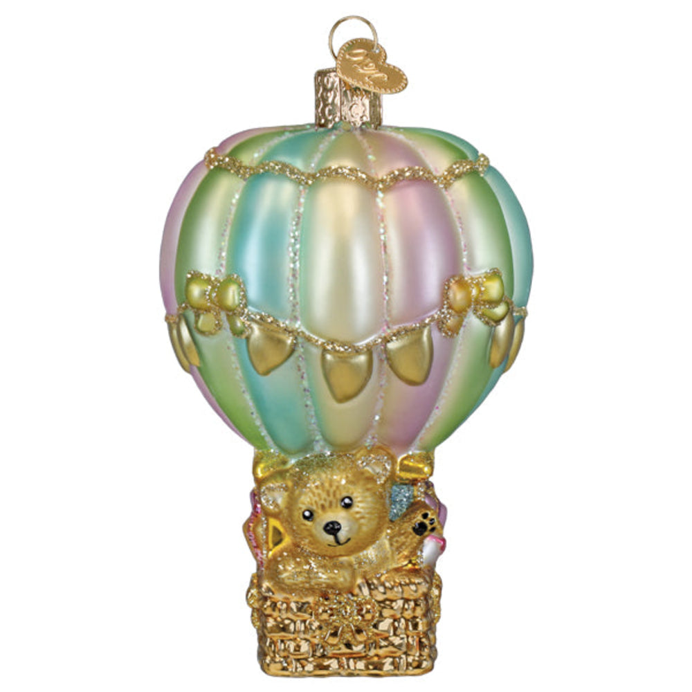 An iridescent hot air balloon Christmas ornament featuring pastel green, pink, and yellow tones with gold glitter trim, a gold hanging loop, and a gold basket carrying a teddy bear at the bottom, shown on a plain white background.