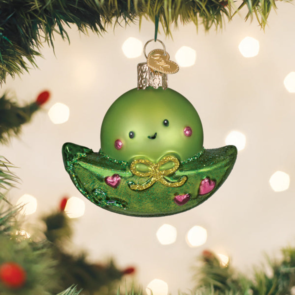 Green glass ornament shaped like a character with a bow, hanging on a Christmas tree.