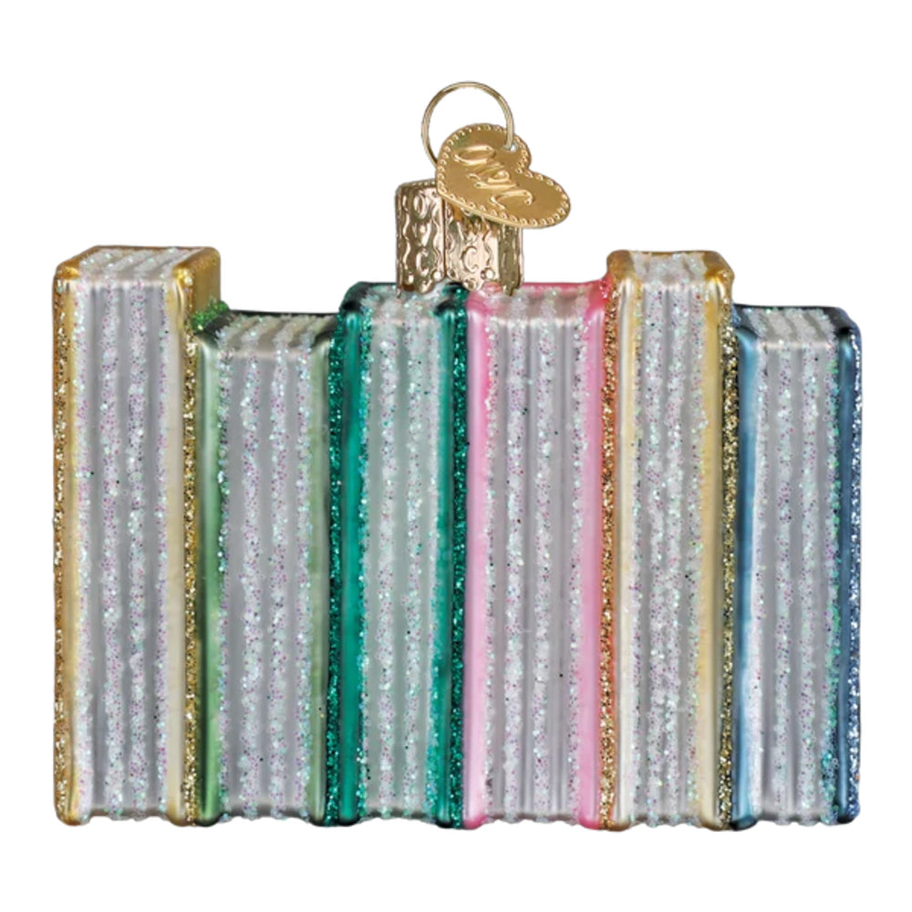 A decorative book-shaped ornament featuring multiple glass books with glittery covers in silver, teal, pink, blue, and gold, topped with a gold hanging loop and tag.