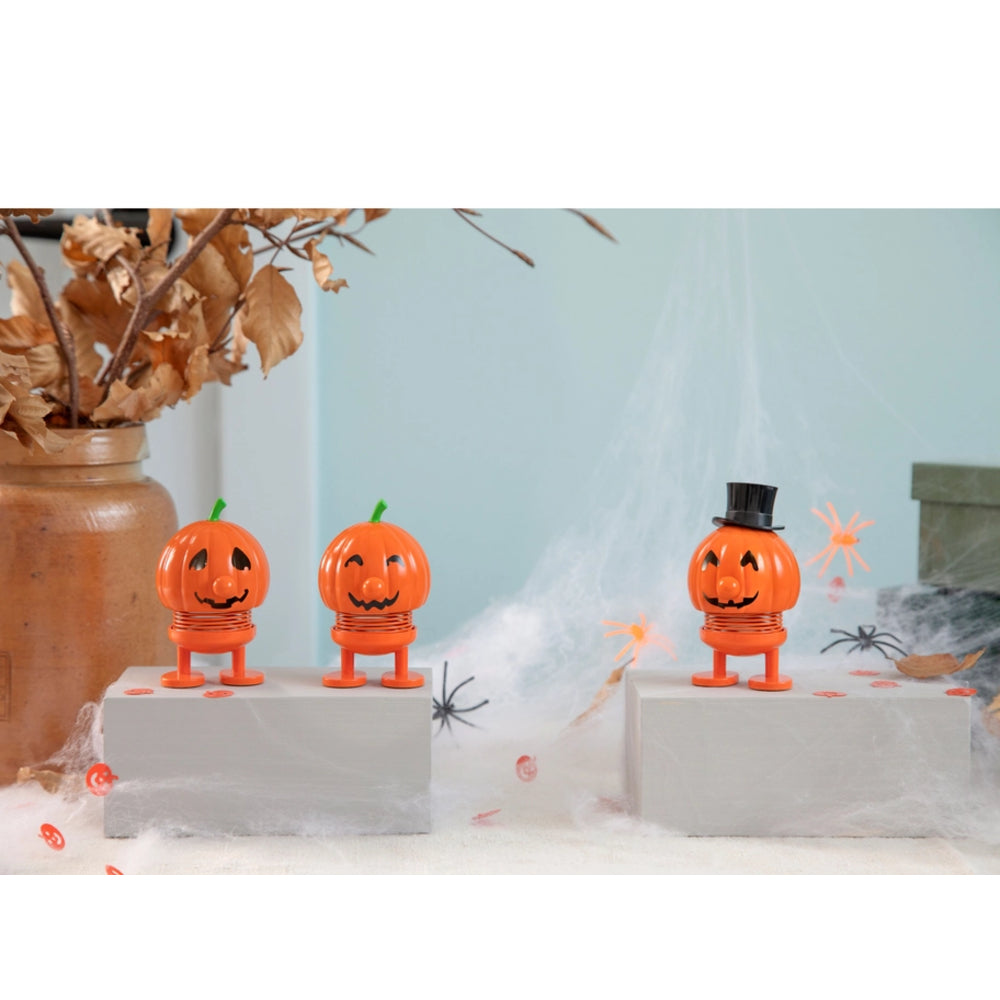 Three small orange jack-o'-lantern Halloween figurines with carved faces stand on gray display blocks. One pumpkin wears a green stem and the other two have black facial cutouts.