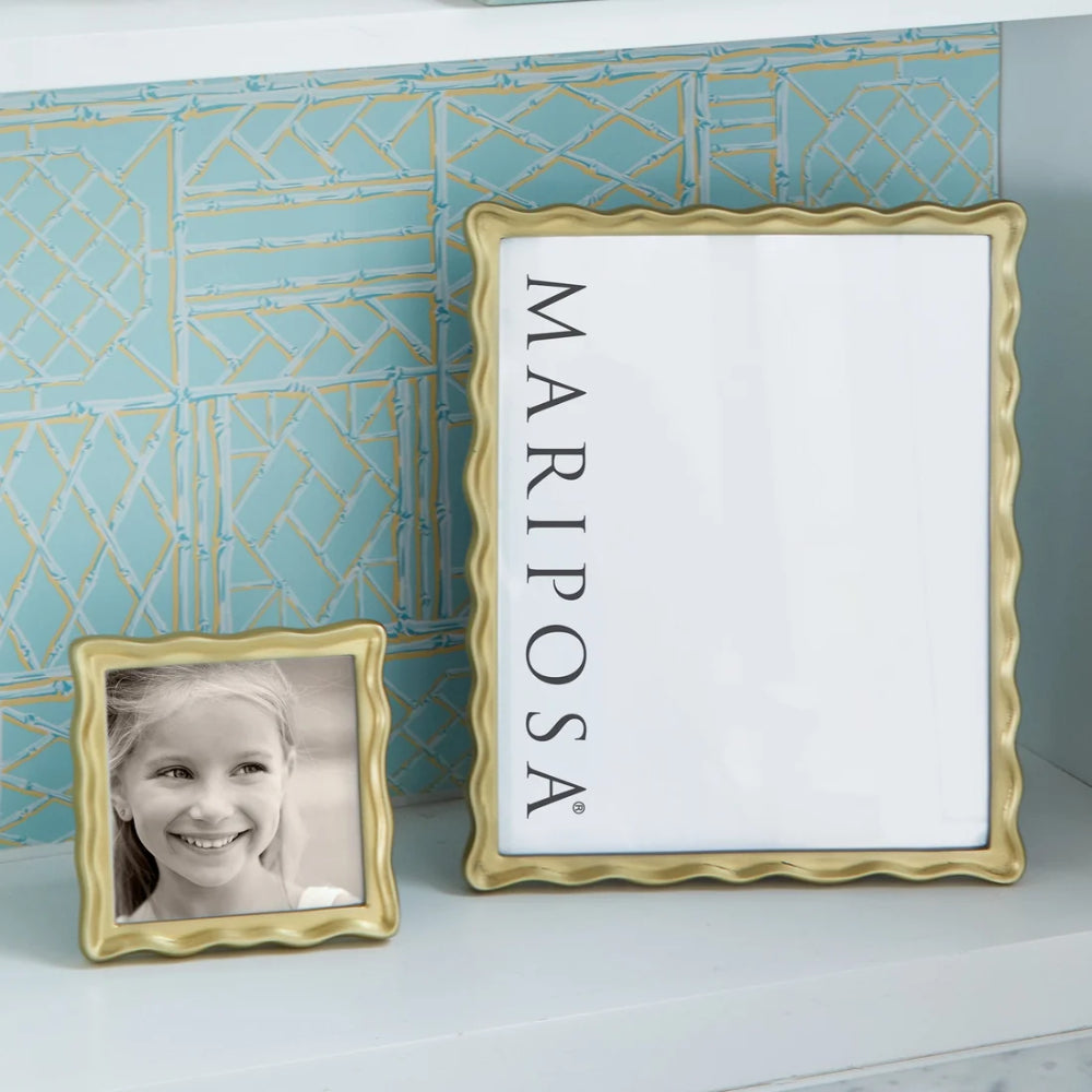 Gold picture frame with a child's photo and 'Mariposa' branding against a decorative blue wall.