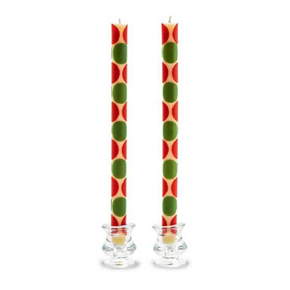 Two candles with red and green polka dot pattern in glass candle holders on a white background
