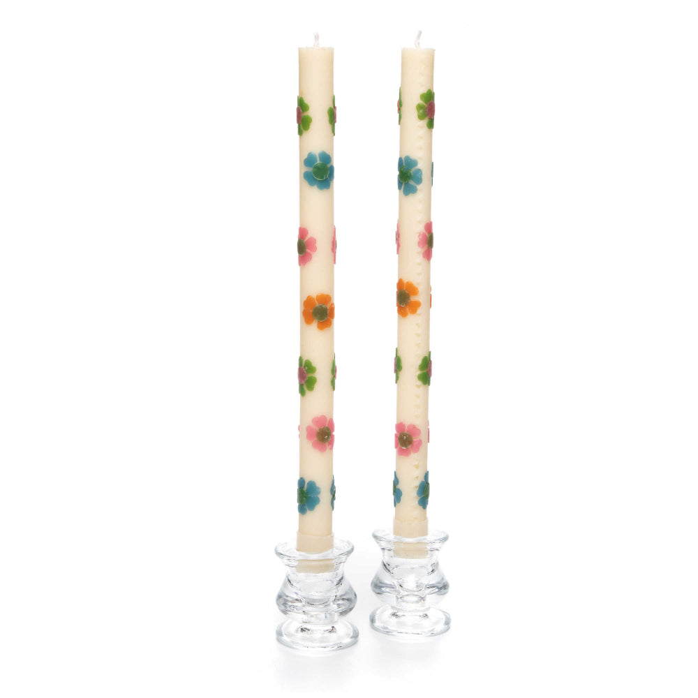 A set of two white white with muilt-colored floral-patterned candles with glass holders on a white background