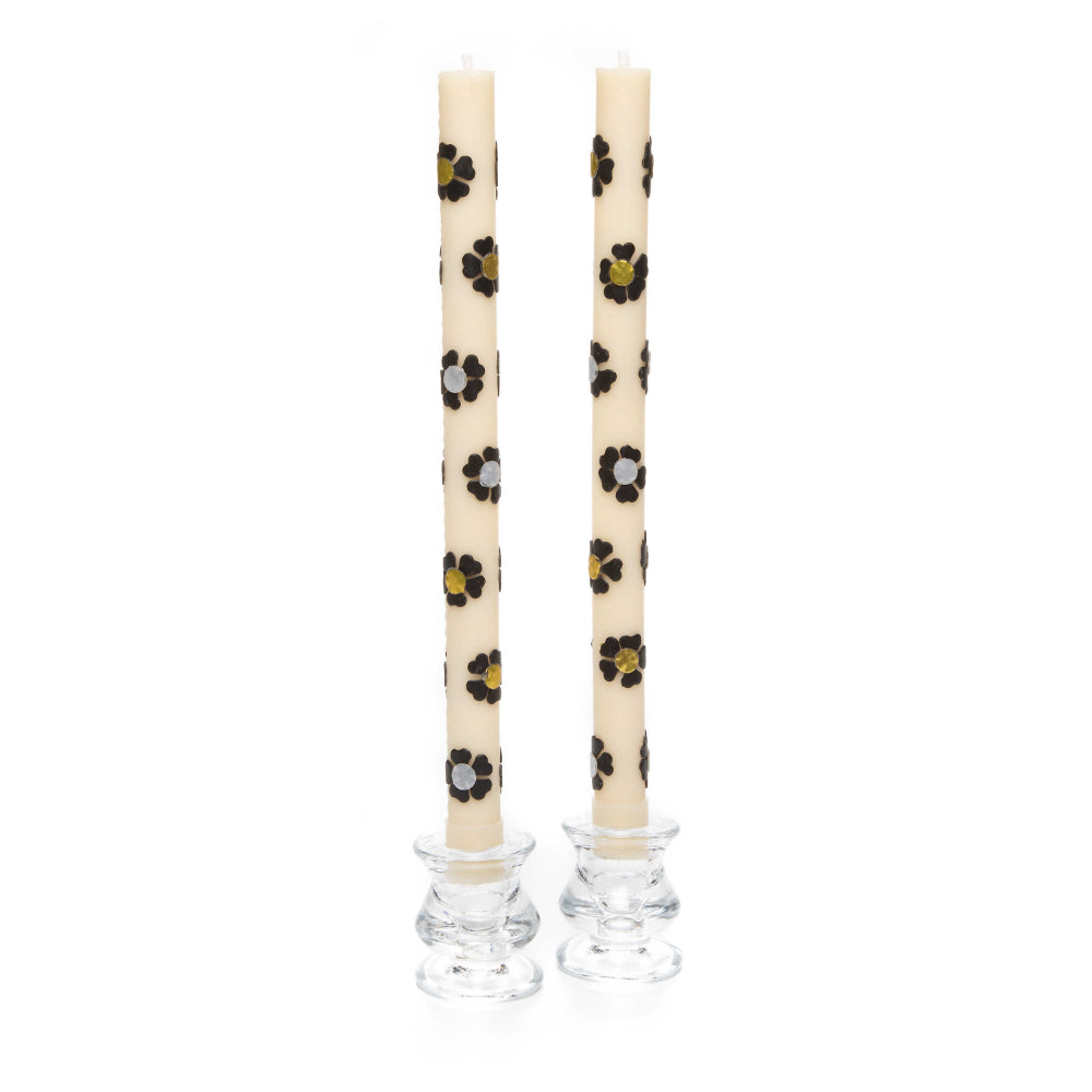 A set of two white with silver & gold colored floral-patterned candles with glass holders on a white background