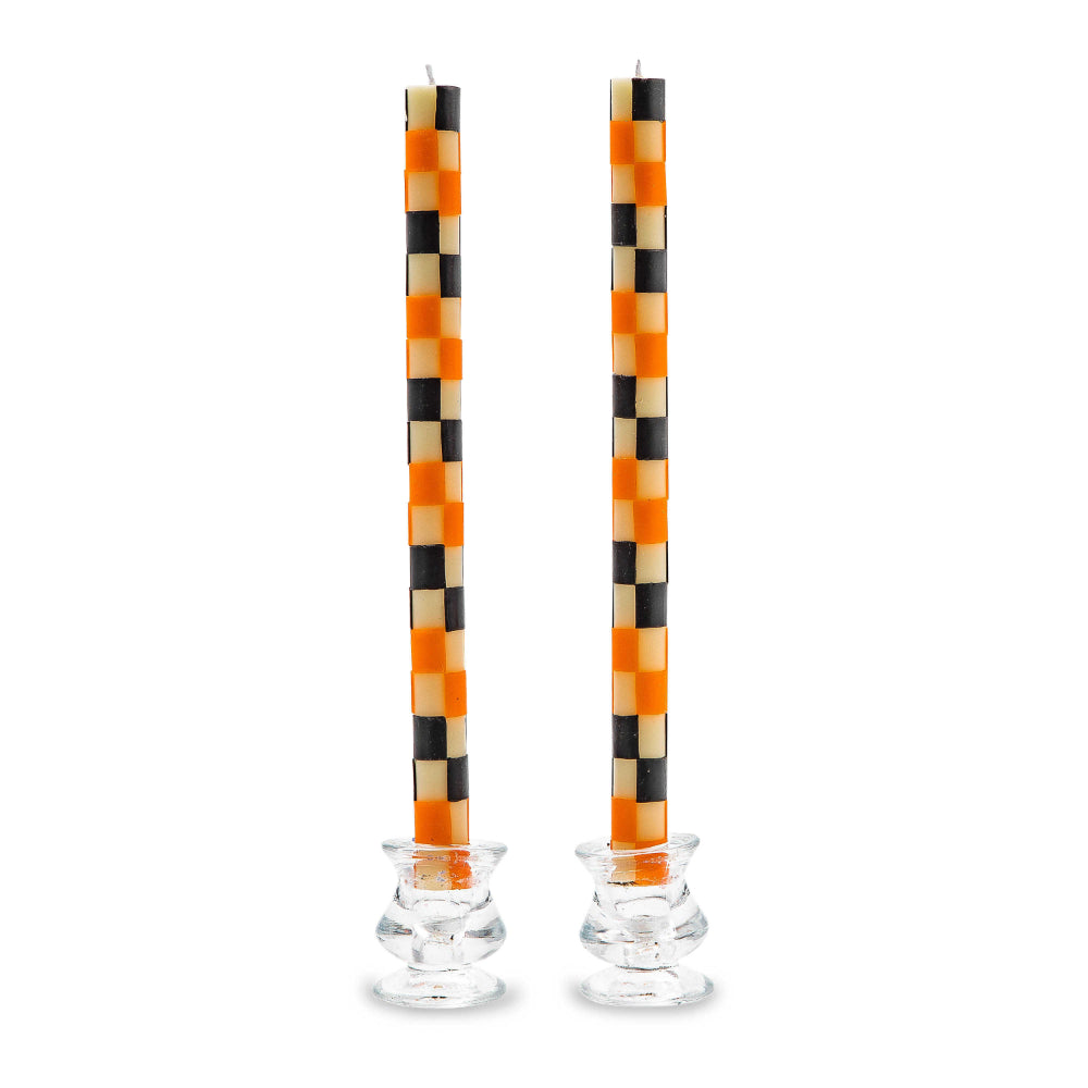 Pair of checkered candles with black, orange, and beige pattern in glass holders on a white background